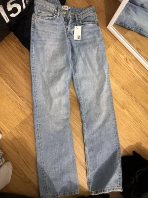 Ljusblå raka jeans från 157 - Säljer ett par ljusblå raka jeans från 157 med klassisk femficksmodell och knappgylf. Jeansen har hög midja och är tillverkade i ett slitstarkt denimtyg. Perfekta för en avslappnad och trendig look. Storlek xs 