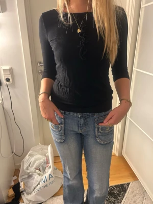 Svart topp med 3/4-ärm och snörning - Snygg svart topp med trekvartsärm och dekorativ snörning framtill. Figurnära passform och rund halsringning. Perfekt att matcha med jeans eller kjol för en trendig look. Materialet ser ut att vara mjukt och stretchigt.