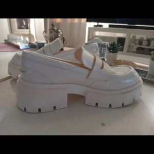H&M loafers med platåsula - Säljer ett par chunky vita loafers med kraftig platåsula och markerad söm. Skorna har klassisk pennyloafers-design och är tillverkade i ett slätt material som liknar läder. Perfekta för dig som vill ha en trendig och stilren look.