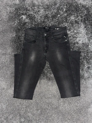 Svarta Replay jeans med tvättad look - Säljer ett par svarta jeans från Replay med snyggt tvättad finish och klassisk femficksmodell. Jeansen har raka ben och silverfärgade detaljer vid fickorna. Perfekta för dig som gillar en avslappnad men trendig stil.