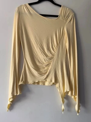 Ljusgul långärmad topp med snörning - Trendig ljusgul topp med långa ärmar och asymmetrisk nederkant. Toppen har snygg snörning i sidan som ger en cool draperad effekt. Materialet känns mjukt och stretchigt, perfekt för dig som gillar unika detaljer.