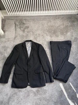 Svart randig kostym från Batistini - Säljer en svart kostym från Batistini. Kavaj + matchande byxor. Stilren och klassisk, passar perfekt till fest, student, bröllop eller jobb.  Storlek:  Kavaj: 46  Byxor: 32/32