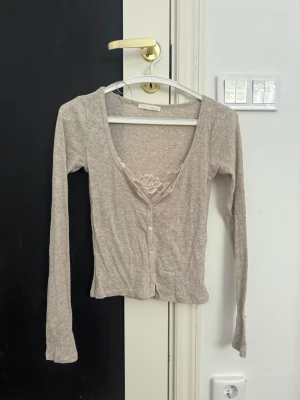 Beige kofta - Superfin beige/taupe cardigan från Zara i storlek S, aldrig använd.  Den virala modellen som synts mycket på sociala medier, med fin spetsdetalj i urringningen, knappar framtill och en feminin, figurnära passform. Perfekt att styla med jeans eller kjol.