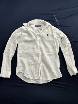 Vit linneskjorta från Polo Ralph Lauren - Klassisk vit skjorta i linne från Polo Ralph Lauren med lång ärm och knappar framtill. Köpt för 3000kr från Zalando och använts 1 gång. Den är ostruken och därför ser ut sådär men den är i nyskick