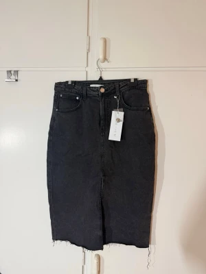 Svart jeanskjol från Amisu - Snygg gråsvart lång jeanskjol från Amisu med klassisk femficksdesign och rå kant nertill. Kjolen har hög midja och en slits framtill. Aldrig använd, köpt i höstas för 299kr. 