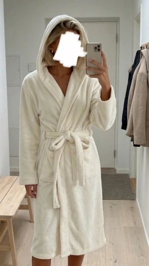 Vit fluffig morgonrock med huva - Mysig vit morgonrock i supermjuk fleece med huva och två stora fickor framtill. Lång modell med knytskärp i midjan, perfekt för att chilla hemma. Enkel och stilren design som känns lyxig och varm.