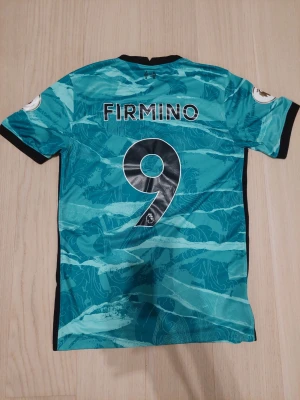 ÄKTA Firmino 9 - ÄKTA Liverpool tröja från stadiumet köpt. Bara bokstäverna I och R håller på att gå av lite. Storlek S. I turkos färg.