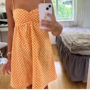 Orange blommig sommarklänning med smala axelband - Superfin orange klänning med vita små blommor och smala axelband. Lätt och luftig modell, perfekt för varma dagar. Söt rynkning vid bysten och kort längd. Perfekt för sommarens alla tillfällen! Kan diskutera pris