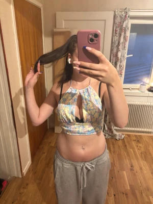 Pastellfärgad croppad halterneck topp - Säljer en croppad halterneck topp i pastellfärgat mönster med blå, rosa, gul och vit. Toppen har en snygg cut-out framtill och är tillverkad i 100% polyester. Perfekt för dig som vill sticka ut med en unik och färgglad stil.