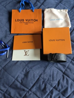 Svart Louis Vuitton bälte i skinn - Snyggt svart bälte från Louis Vuitton med klassiskt LV-spänne i metall. Bältet är gjort i strukturerat skinn och har en stilren design som passar till många outfits. Levereras med originalförpackning och dustbag.