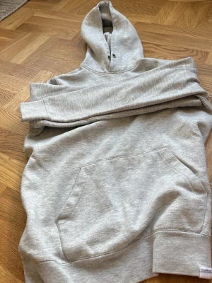 Grå hoodie från Pull&Bear - Säljer en ljusgrå hoodie från Pull&Bear i storlek S. Hoodien har en klassisk känguruficka framtill, ribbade muddar och en stor huva med dragsko. Perfekt för chill dagar och enkel att matcha med jeans eller mjukisbyxor.
