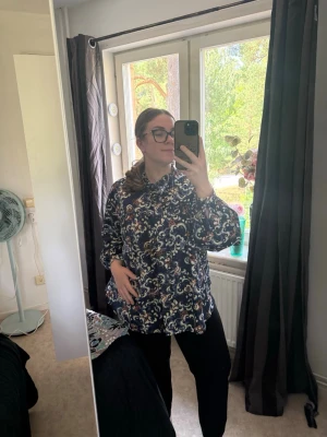 Mönstrad blus med volangkrage - Säljer en snygg blus med mörkblå botten och vitt, beige samt brunt blommönster. Blusen har volangdetaljer vid kragen och knäppning framtill. Passar perfekt till både jeans och kostymbyxor. Materialet känns lätt och luftigt. Knappar ända ner. Från märket Odd Molly i storlek 4 som enligt deras storlekguide motsvarar en storlek XL. Mycket fint skick, jag hittar inga synliga anmärkningar eller defekter. 