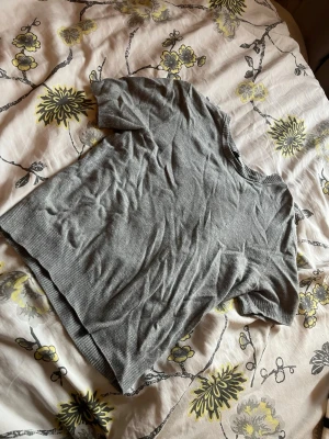 Grå kortärmad stickad tröja - En enkel och stilren grå stickad tröja med korta ärmar och rund hals. Tröjan har ribbade muddar vid ärmslut och nederkant, vilket ger en snygg finish. Perfekt att matcha med jeans eller kjol för en avslappnad look. Tröjan är från h&m men prislappen är borta.
