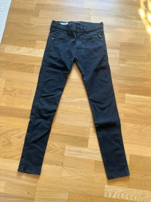 Replay svarta jeans slim fit - Säljer ett par svarta slim fit jeans med fem fickor och hög midja. Jeansen har en klassisk design med bälteshällor och knappgylf. Materialet är stretchigt för extra komfort och passform. Perfekta till en avslappnad eller trendig look.