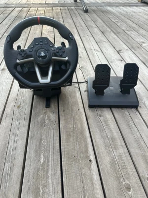 Ratt och pedaler till PlayStation - Säljer en gamingratt med pedaler för PlayStation dator och allt annat med USB. Ratten är svart med detaljer i silver och har PlayStation-knappar, styrkors och paddlar. Pedalerna är svarta och kopplas ihop med ratten. Perfekt för racing- och bilspel för en mer realistisk spelupplevelse.