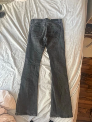 Grå bootcut jeans med rå kant - Säljer ett par grå bootcut jeans med rå kant nertill. Jeansen har klassisk femficksdesign och normal midja. Materialet är denim i bomull med lite stretch för skön passform. Perfekta för dig som gillar en avslappnad men ändå trendig look.