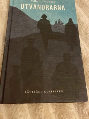 Utvandrarna av Vilhelm Moberg - En lättläst klassiker av Vilhelm Moberg, återberättad av Cecilia Davidsson. Boken har hårda pärmar med ett omslag i blått och svart, prydd med silhuetter av människor och ett skepp. Första delen i en serie om svensk utvandring till Amerika.