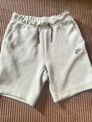 Gråa Nike shorts med snörning - Gråa shorts från Nike i mjukt sweatshirtmaterial. De har elastisk midja med svart snörning och två sidofickor. Perfekta för träning eller chill och har en stilren look med Nike-logga på benet.