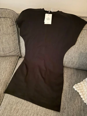 Svart kortärmad klänning - En enkel och stilren svart klänning i kort modell med korta ärmar och rund hals. Tillverkad i mjuk bomull som känns skön mot huden. Perfekt för dig som gillar minimalistisk och clean stil. Oanvänd.