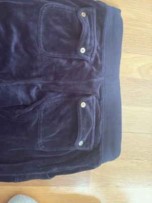 Juicy couture  - Säljer ett par mörkblå juicy byxor i mjuk velour med bred resår i midjan och dragsko. Byxorna har två stora fickor fram med lock och silverfärgade knappar. Perfekta för chill dagar eller när du vill vara extra bekväm.