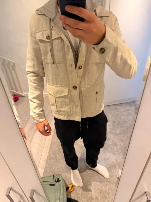Beige linnéovershirt   - Stilren beige overshirt i linnematerial med fyra stora fickor framtill och knappar i trälook. Klassisk krage och långa ärmar med knappdetaljer vid ärmslut. Perfekt för en avslappnad men snygg look. Nypris 1599 mitt pris 649