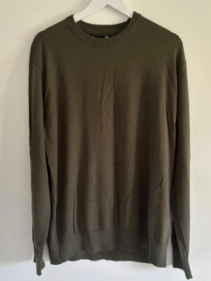 Olivgrön basic tröja med rund hals - En enkel och stilren olivgrön tröja med rund halsringning och långa ärmar. Tröjan har en rak passform och ribbade muddar vid ärmslut och nederkant. Perfekt att matcha med jeans eller över en skjorta.