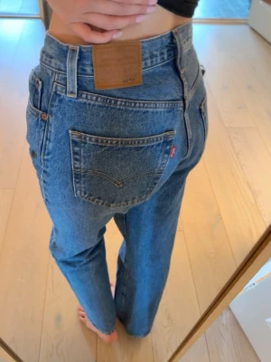 Blå raka jeans från Levi's - Klassiska blå jeans från Levi's med rak passform och hög midja. Jeansen har fem fickor, synliga sömmar och en brun läderpatch bak i midjan. Tillverkade i denim med en tidlös look och ikonisk röd Levi's-tagg på bakfickan.
