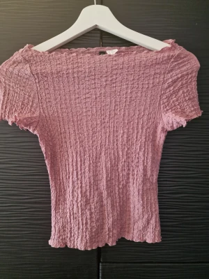 Rosa smockad topp från Divided H&M - Säljer en ljusrosa smockad topp från Divided H&M. Toppen har korta ärmar, offshoulder-design och stretchigt tyg som formar sig efter kroppen. Perfekt för dig som gillar en feminin och trendig stil.