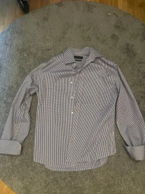 Blårutig skjorta från Riley - Klassisk blårutig skjorta från Riley i bomull. Skjortan har lång ärm, knappar framtill och en snygg krage. Perfekt för en clean och stilren look. Passar till jeans eller chinos.