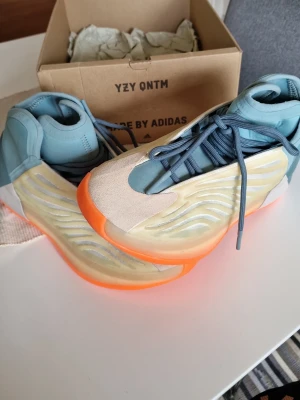 YZY QNTM sneakers med orange sula - Unika YZY QNTM sneakers från Adidas med futuristisk design. Skorna har ljusblå ovandel, beige meshpaneler och en iögonfallande orange sula. Materialmix av textil, mesh och syntet. Perfekta för dig som vill sticka ut med din sneakers till. *använda 1 gång för test * stl 43