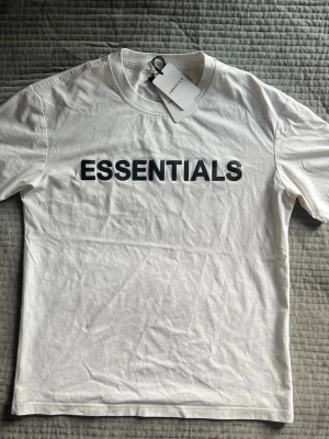 Essentials T-shirt - Essentials T-shirt i vit med stilren svart ESSENTIALS-logga över bröstet. Enkel och clean modell som passar till både jeans, shorts och andra outfits.  Storlek: xs/s  Skick: helt ny  Tags/lappar kvar 