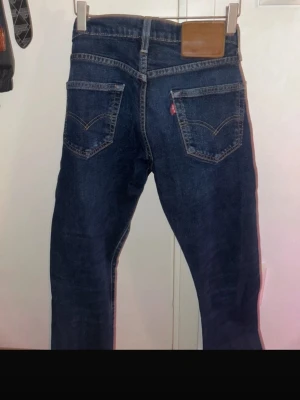 Levis jeans - Säljer ett par klassiska mörkblå jeans med rak passform och fem fickor. Jeansen har kontrastsömmar, bälteshällor och knappgylf. Perfekta till vardagslooken och passar till det mesta. Materialet är denim i bomull. 502, W 28 L32