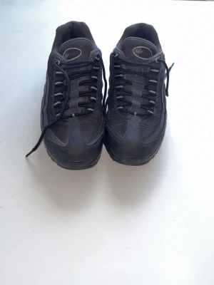 Nike Air Max 95 - Black Nike Air Max trainers in a classic all-black design. Comfortable cushioned sole, mesh and synthetic upper, lace-up fastening, and Nike Air branding on the tongue and heel. 