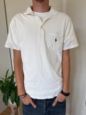 Vit kortärmad skjorta från Polo Ralph Lauren - Vit skjorta från Polo Ralph Lauren med korta ärmar och klassisk krage. Skjortan har en bröstficka med den ikoniska loggan broderad i blått. Tillverkad i mjuk bomull och har knappar framtill.