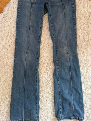 Blå bootcut jeans med kontrastsömmar - Ett par klassiska blå bootcut jeans med tydliga kontrastsömmar längs benen. Jeansen har fyra fickor och normal midja. Materialet är denim i bomull och passformen är avslappnad, stretch med lätt utsvängda ben.