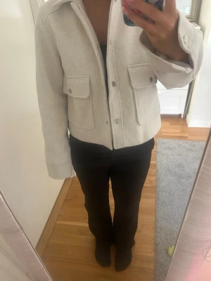 Beige kappa  - Snygg beige overshirt med stora bröstfickor och tryckknappar framtill. Jackan har en rak, lite boxig passform och klassisk krage. Perfekt att slänga över en hoodie eller t-shirt för en chill look.