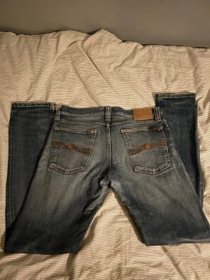 Nuddie jeans  - Snygga blå jeans med klassisk femficksdesign och broderade detaljer på bakfickorna. Jeansen har en något tvättad look och raka ben. Perfekta för en avslappnad stil och passar till det mesta i garderoben. Hör av er vid frågor😃