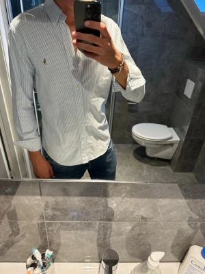 Vit och blårandig skjorta Ralph lauren - En snygg blå och vit randig Ralph Lauren skjorta. En klassisk skjorta som alltid funkar. Skjortan är i stort sett bra skick bortsett från ett litet lite hål på ryggen. Hålet syns knappt se näst sista bild men kollar man när som på sista bilden så syns det. Jag på bilden är 188cm och bär strlk M. Hör  av er vid fler frågor o funderingar;)