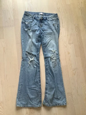 Ljusblå slitna bootcut jeans Gina Tricot - Säljer ett par low waist ljusblå bootcut jeans från Gina Tricot med slitningar och hål på båda benen. låg midja och är tillverkade i denim. Supersnygga och perfekta nu till hösten.