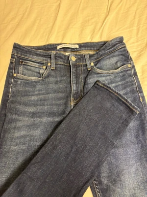 Blå jeans från Calvin Klein - Säljer ett par klassiska blå jeans från Calvin Klein Jeans. Jeansen har fem fickor, snygga kontrastsömmar och ett stort logopatch bak i midjan. Materialet är stretchigt denim som sitter med bra passform och bekvämt. Perfekta till vardagslooken!