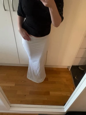 Vit långkjol i stretchigt material - Säljer en enkel och stilren vit långkjol med figurnära passform. Kjolen är rak i modellen och har en mjuk, stretchig känsla som gör den bekväm att bära. Perfekt att matcha med en crop top eller en oversized tröja.