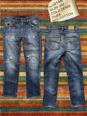 *Bootcut* Nudie ”Slim Jim” med Slitningar - Ett par helt sjuka nudie jeans i deras absolut bästa modell enligt mig, ”Slim Jim”, som sitter med en diskret bootcut! Extremt fina slitningar på detta par. Annan storlek på lappen men passar enligt mig 32/32. Mått på sista bilden. Hör av dig vid frågor!
