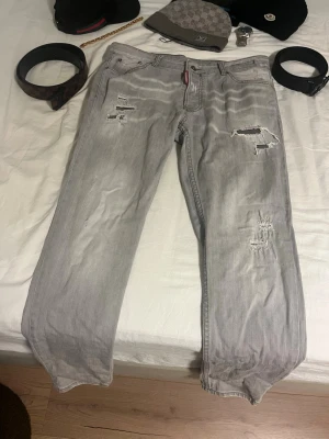 D2 jeans - Säljer ett par ljusgrå jeans med flera slitningar och hål på både fram- och baksidan. Jeansen har raka ben och klassisk femficksmodell. Perfekta för en avslappnad och trendig streetwear-look.