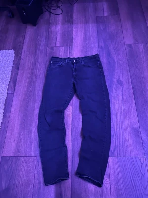Svarta levis jeans - Säljer ett par svarta slim fit jeans med klassisk femficksdesign och knappgylf. Jeansen har raka ben och subtila sömmar. Passar perfekt till en avslappnad och trendig stil. Materialet känns mjukt och stretchigt för extra komfort.