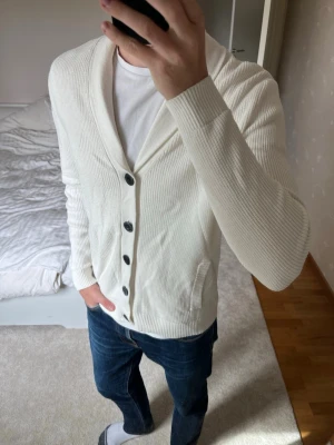 Vit cardigan med knappar från Hollister - Säljer en sjukt fet stickad cardigan från Hollister gjord i ett väldigt skönt material. Cardiganen är i ett väldigt fint skick utan defekter! ✌🏼——————————————————————————                                                                      📐| Storlek: M                                                           👖| Märke: Hollister                                                🔎| Skick: Mycket Fint!                                                     ✍🏻| Skriv om du har några frågor
