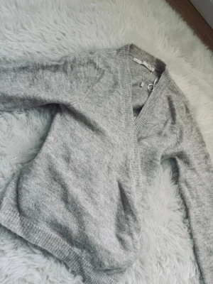 beige omlottstickad tröja - mysig beige stickad tröja med omlott-design och bred ribbad kant vid halsen. Tröjan har långa ärmar och är gjord i ett mjukt material som känns skönt mot huden. Perfekt för hösten! 💆🏼‍♀️