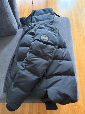 Vinterjacka Black Label - Säljer en svart dunjacka  med huva och black label logotyp på ärmen. Jackan har en klassisk puffer-design och är fodrad med dun för extra värme. Perfekt för kalla vinterdagar och har praktiska dragkedjefickor och en innerficka samt dragkedja framtill.
