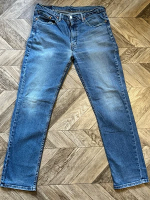 Levi's 514 - Klassiska blå jeans från Levi's med rak passform och fem fickor. Jeansen har en ljus tvätt med subtila slitningar och är tillverkade i bomull. Perfekta för en avslappnad och tidlös stil. Längd 110cm Bredd 42cm