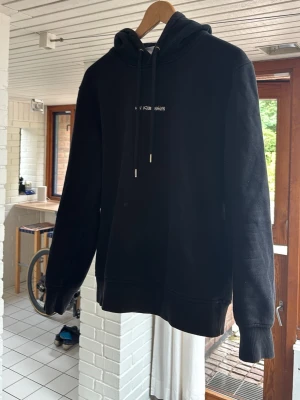 Han Kjobenhavn hoodie - En svart hoodie med huva och dragsnören. På bröstet finns en liten broderad text i vitt. Hoodien har ribbade muddar vid ärmar och nederkant. Perfekt för en chill och avslappnad stil.
