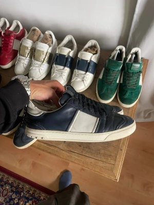 Mörkblåa Valentino Flycrew  - Snygga mörkblåa sneakers från Valentino med vita detaljer och svart snörning. Skorna har en klassisk låg siluett och är tillverkade i läder med en vit sula. Perfekta för dig som vill ha en stilren och exklusiv look.